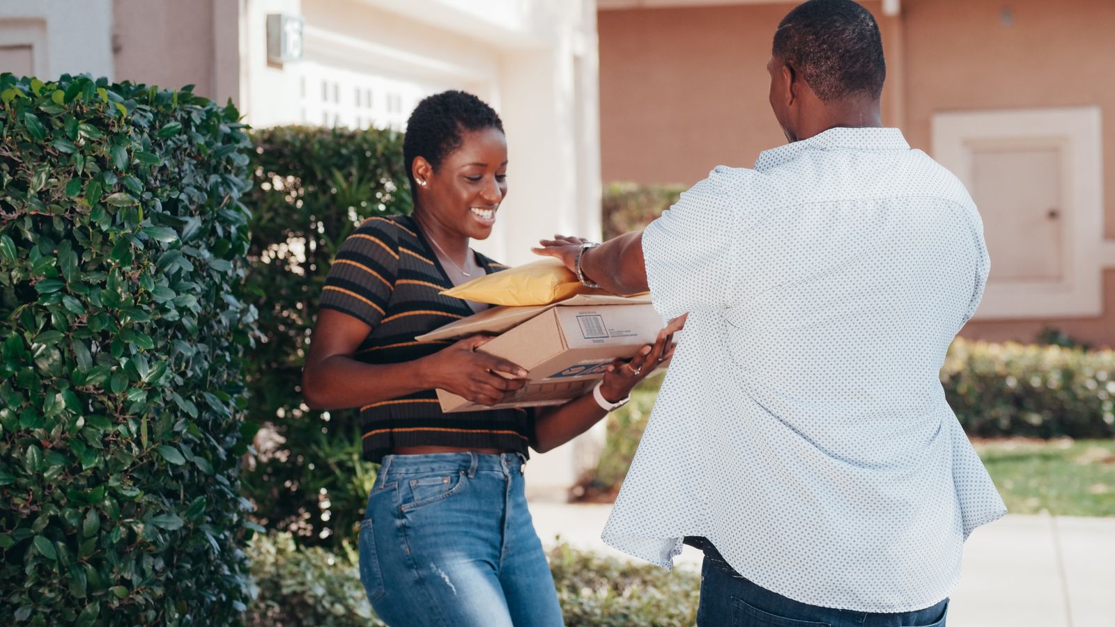 A woman smiling as she receives a parcel outside a home