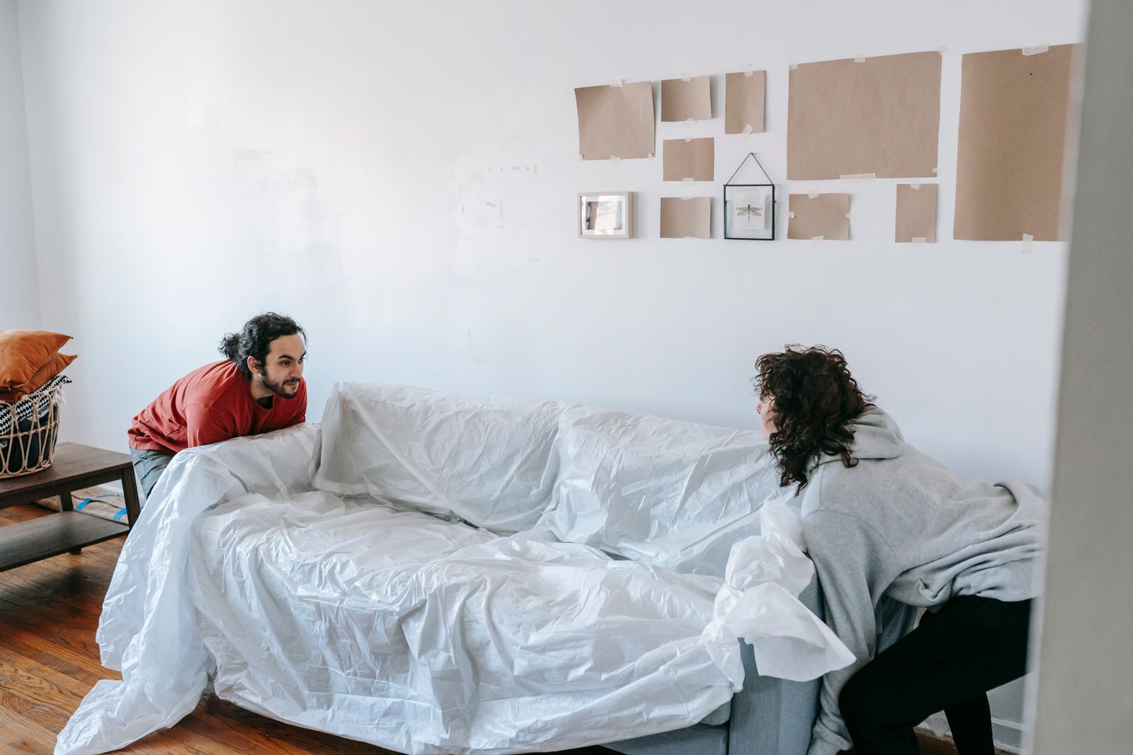 Two people covering a sofa with a protective sheet for moving