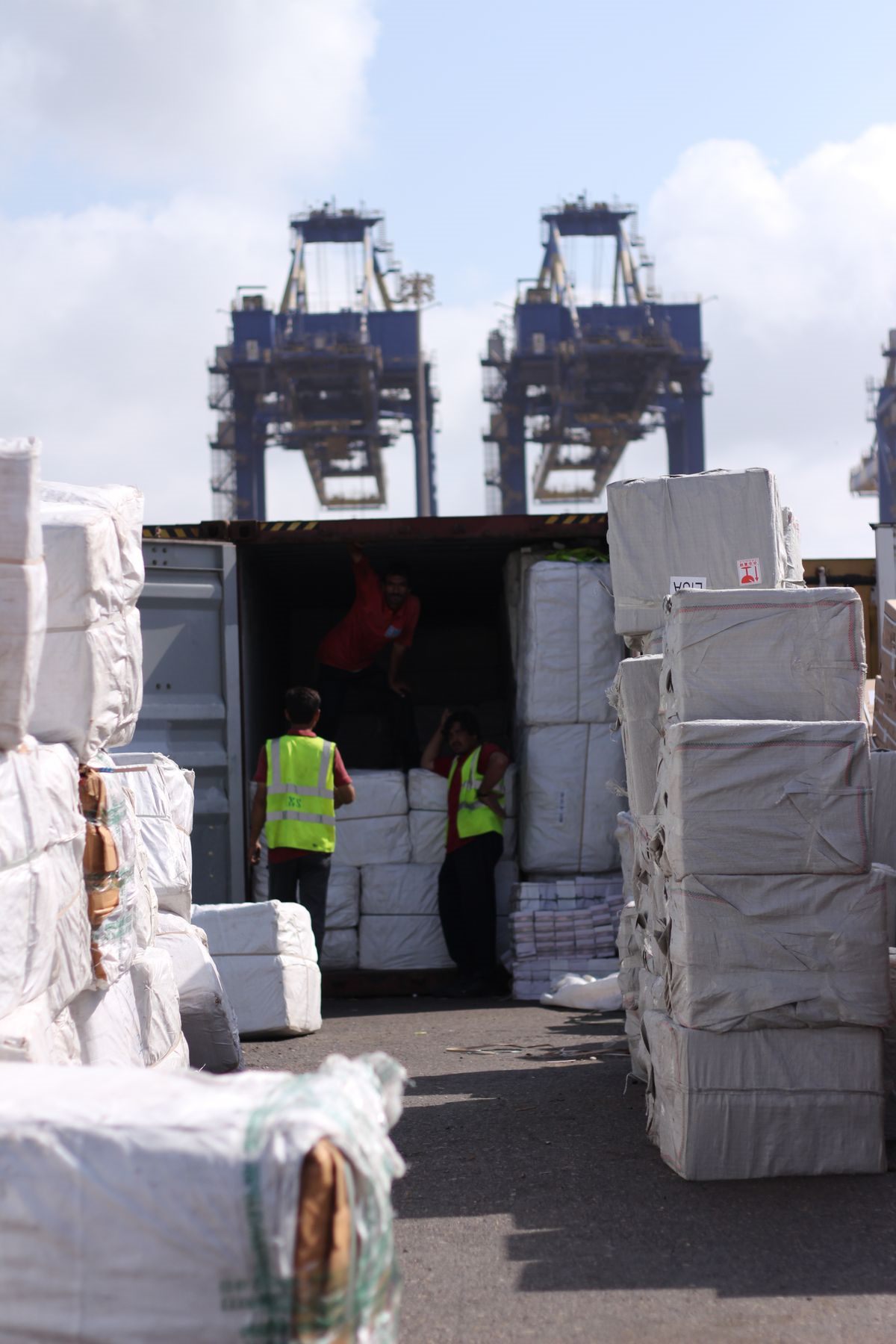 Workers loading wrapped cargo into a shipping container at a port